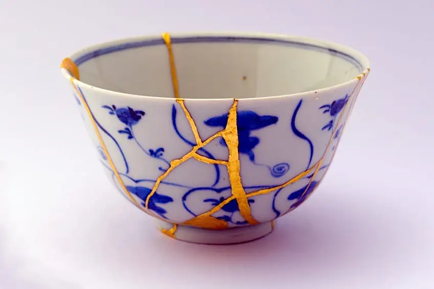 A blue-and-white porcelain bowl with hand-painted cobalt botanicals, broken and repaired with veins of gold using the Japanese kintsugi technique.